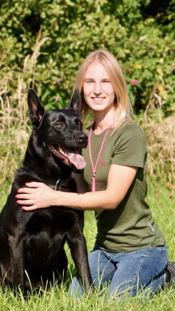 Hundetrainerin Sabine Seifert kniet neben einem schwarzen Hund.